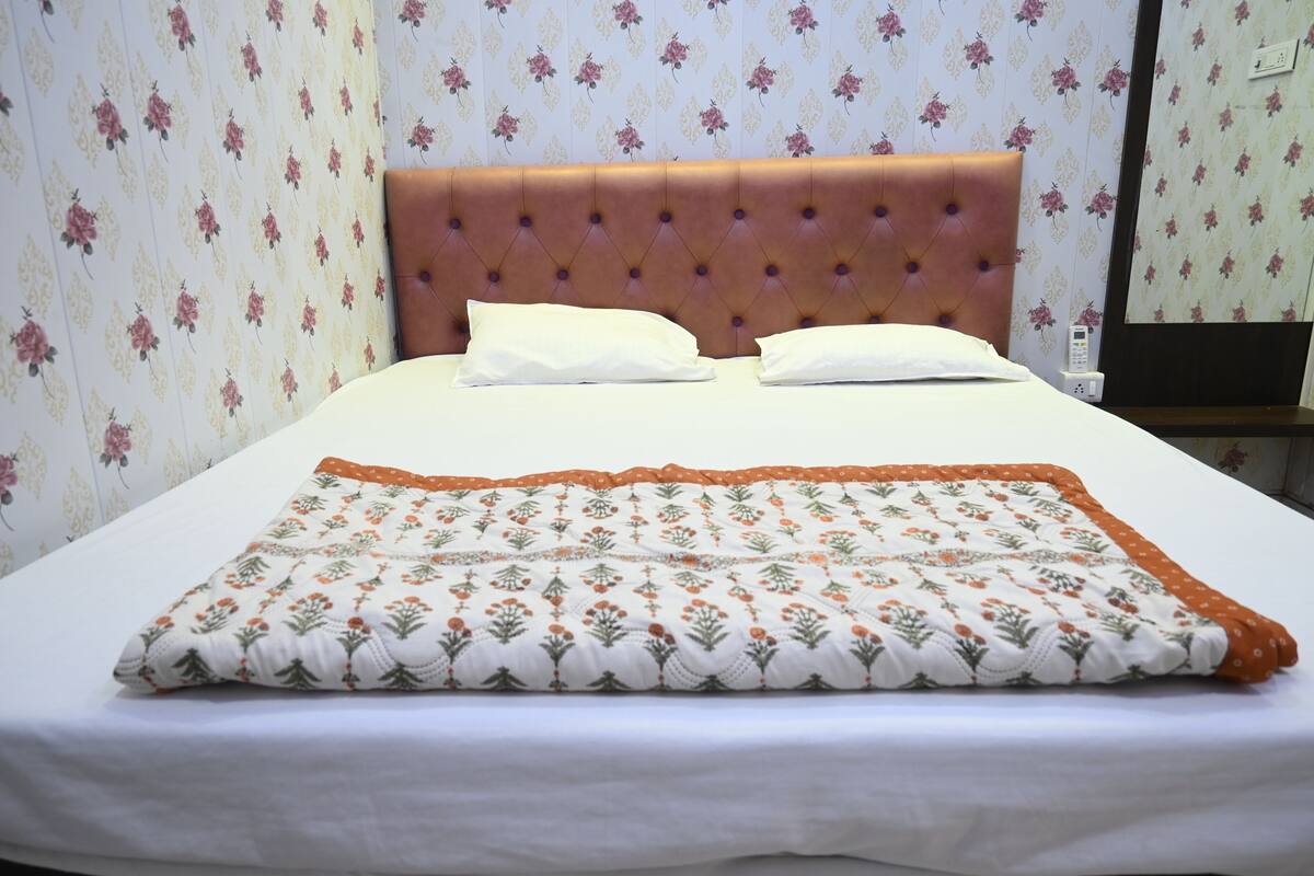 Un lit bien fait, avec une couverture et des oreillers à motifs floraux, une tête de lit capitonnée et un papier peint floral.