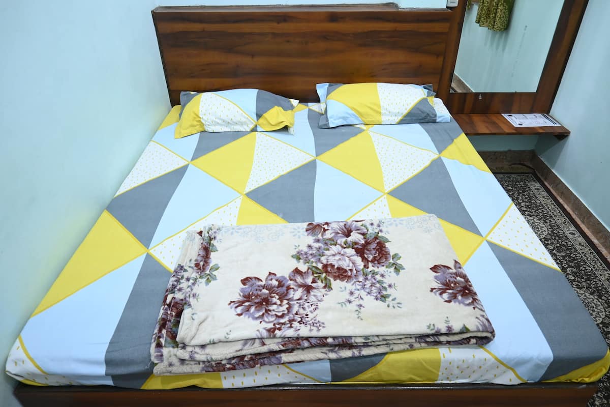 Un lit bien fait, avec une couvre-lit à motifs géométriques et un plaid à fleurs, une tête de lit en bois et une petite table de chevet avec une lampe.