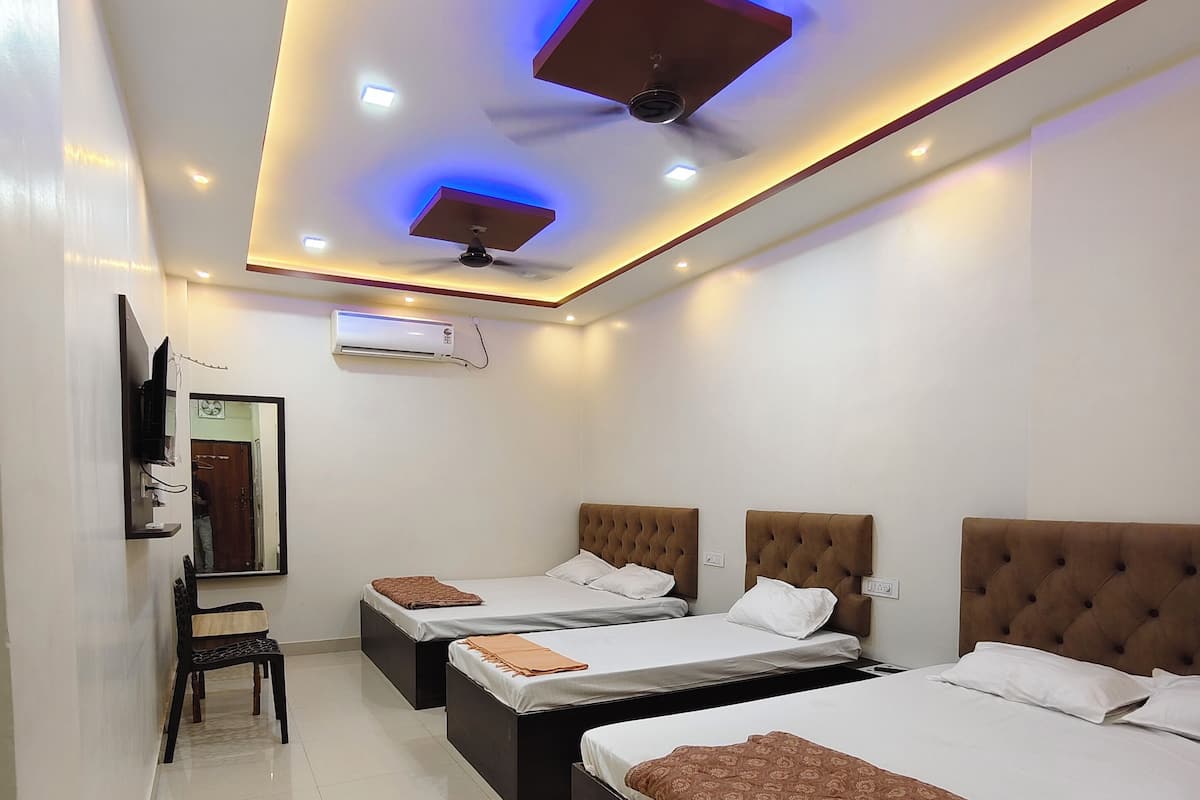 Une chambre d’hôtel avec trois lits, un téléviseur à écran plat, un climatiseur et un ventilateur de plafond.