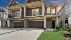 Une maison de ville à deux étages avec un balcon, un garage et une pelouse bien entretenue.