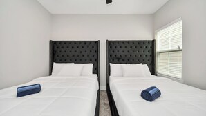 Une chambre d’hôtel avec deux lits, chacun doté d’une tête de lit noire à motifs capitonnés, de draps blancs et d’une serviette bleue.