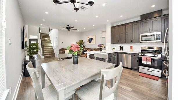 Une cuisine moderne avec un coin repas, comprenant une grande table en bois, des chaises blanches et un ventilateur de plafond.