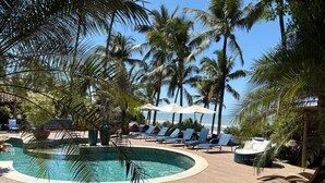 A pool area with lounge chairs and umbrellas, surrounded by palm trees and a view of the ocean. - Pousada Morro dos Navegantes (Ilhéus)