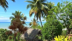 A garden with a thatched-roof structure, palm trees, and a view of the ocean. - Pousada Morro dos Navegantes (Ilhéus)