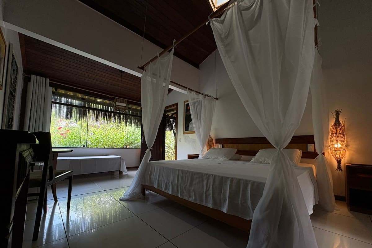 Une chambre à coucher avec un lit sous un dais, un bureau et une fenêtre donnant sur un paysage verdoyant.