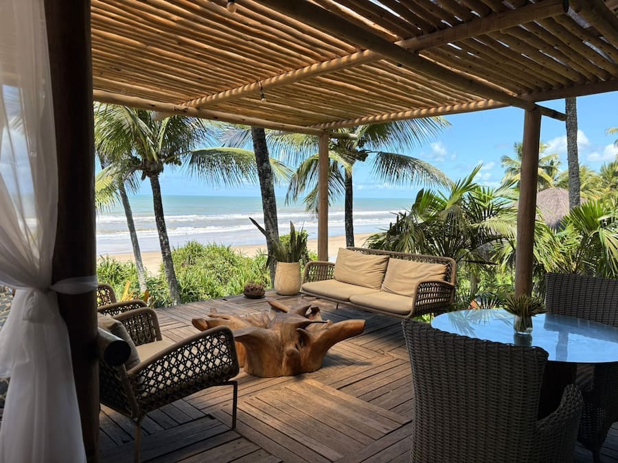 A wooden deck with wicker furniture, a glass table, and a view of the beach and ocean.