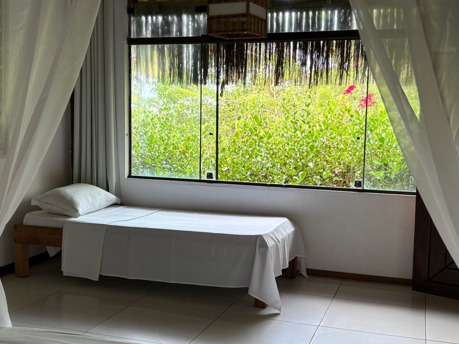 A bedroom with a bed, a window with curtains, and a view of greenery outside.
