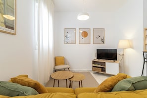 A living room with a sofa, a small table, a TV, and artwork on the wall.
