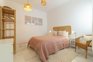 Un dormitorio con cama, mesita de noche, silla y estante en la pared.