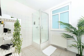 Un baño moderno con cabina de ducha de vidrio, paredes de azulejos blancos, una ventana con vistas y una planta en maceta.