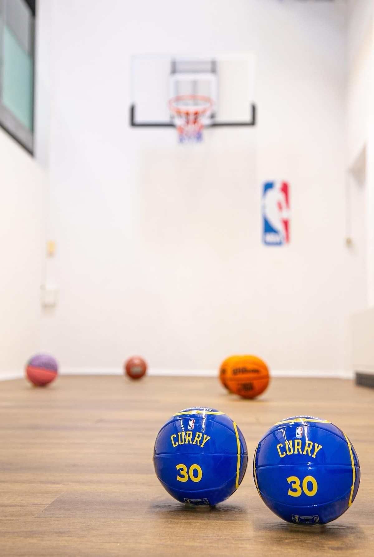 Kaksi koripalloa, joissa on merkintä ”CURRY 30”, puulattialla, ja taustalla näkyy koripallokehä.