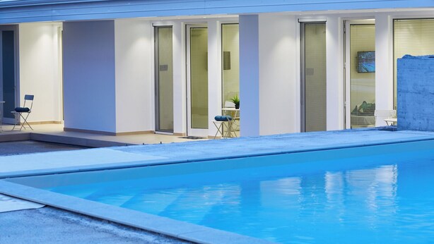 En moderne bygning med swimmingpool, store vinduer og udendørs siddepladser.