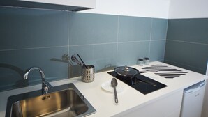Et moderne køkken med en stålvask, en sort induktionskogetop og en hvid bordplade.