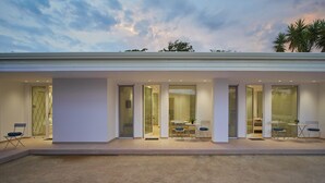 Et moderne hus med en overdækket patio med spisebord og stole, store glasdøre og udsigt til palmer.