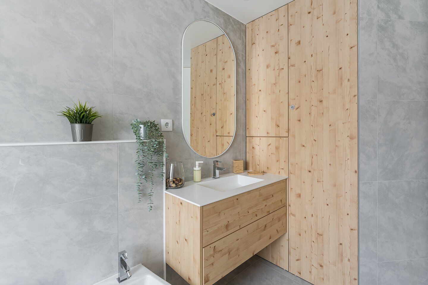 A modern bathroom with a wooden vanity, a large mirror, and a small plant on the shelf.
