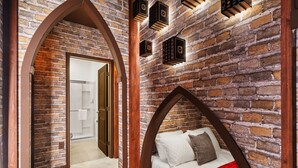 Ein Schlafzimmer mit Backsteinwand, einem hölzernen Bogen und einem Bett mit roter Decke.