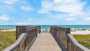 A wooden boardwalk leading to a beach with umbrellas and people in the distance.