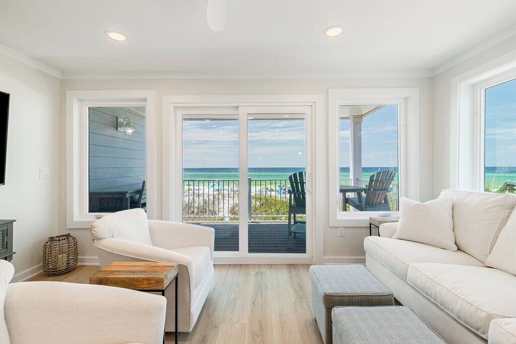 A spacious living room with a large sliding glass door leading to a balcony with a view of the beach.