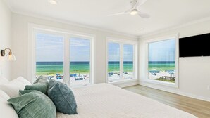 A bedroom with a large bed, multiple windows with a beach view, a ceiling fan, and a mounted TV. - 30A Beachfront | Pool  | Spooky Palms  | Sleeps 10 | Gulf View (Santa Rosa Beach)