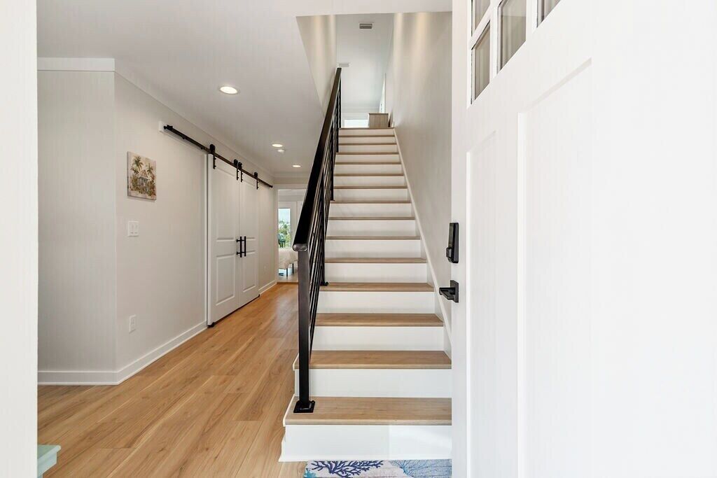 A modern interior with a wooden staircase, white walls, and a kitchen area with cabinets.