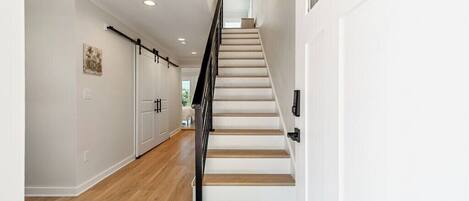 A modern interior with a wooden staircase, white walls, and a kitchen area with cabinets.