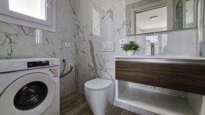 Ein modernes Badezimmer mit Marmor-Spritzschutz, einer Waschmaschine, einer Toilette und einem Holz-Waschtisch mit Spiegel.
