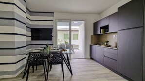 Eine moderne Küche mit grauen Schränken, einem eingebauten Backofen und einem Essbereich mit einem Glastisch und schwarzen Stühlen.