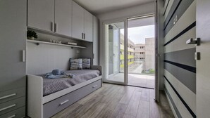 Ein kleines Schlafzimmer mit integriertem Bett, Stauraumschränken und einer Glastür zum Balkon.