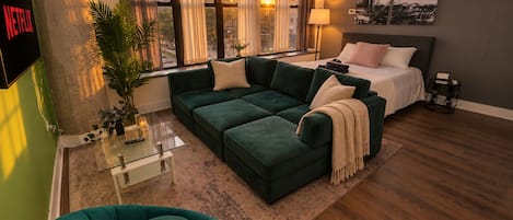 A modern living room with a sectional sofa, a small round table, and a bed with a headboard.