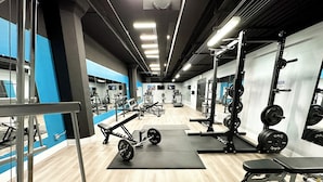 Ein Fitnessstudio mit verschiedenen Trainingsgeräten, darunter Gewichtbänke, Kniebeugeständer und Laufbänder.