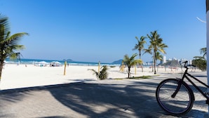 Ein Strand mit einem Fahrrad, das am Gehweg steht, Palmen und einem strahlend blauen Himmel.