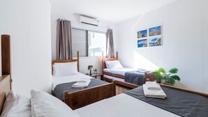 Ein Hotelzimmer mit zwei Einzelbetten, einem Fenster mit Vorhängen, einer Wandklimaanlage und einem kleinen Tisch mit einer Lampe.