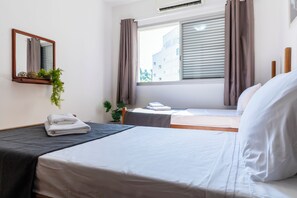 A hotel room with two beds, a window with blinds, a mirror, and a small plant on the wall. - 250m da praia com AC 4 quartos (Guaruja)