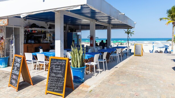 Ein Straßencafé mit Tischen und Stühlen, einer Kreidetafel mit Speisekarte und Blick auf das Meer.