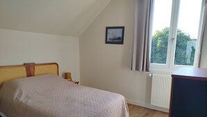 A bedroom with a bed, a nightstand, a picture on the wall, and a window with curtains.