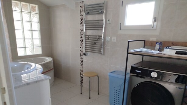 A compact laundry room with a washing machine, a drying rack, a sink, and a window.