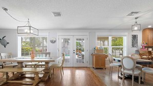 A spacious dining area with wooden tables and chairs, a large window with blinds, and a ceiling fan.