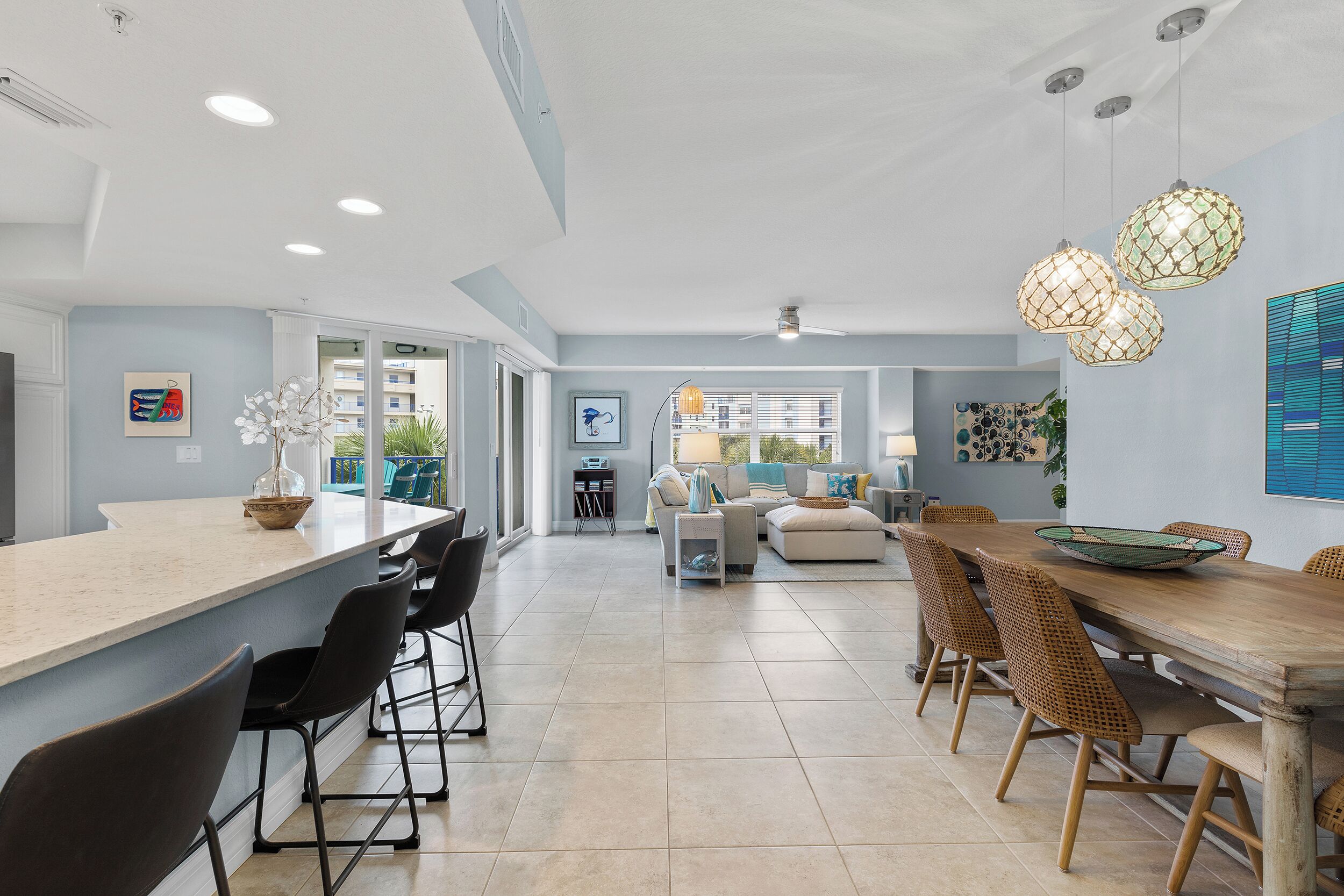 A modern kitchen with a large island, bar stools, and a dining area with a wooden table and wicker chairs.