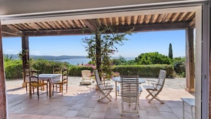 An outdoor patio with a pergola, a table with chairs, and a view of the sea.