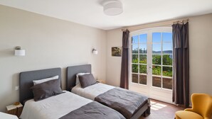 A bedroom with two beds, a chair, and a window with curtains.