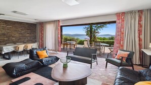 A modern living room with a stone wall, leather sofas, a coffee table, and a view of a vineyard.