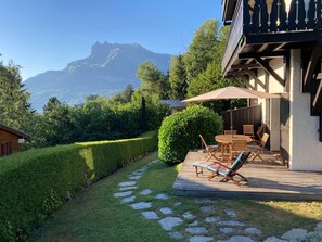 A wooden deck with outdoor furniture, a stone pathway, and a view of a mountain range.