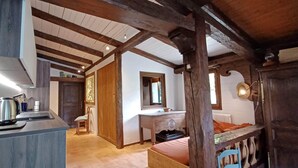 A rustic kitchen with wooden beams, a countertop with a kettle, and a chair.
