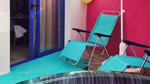 A small outdoor area with a hot tub, two green lounge chairs, a white umbrella, and a red wall.