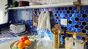 A kitchen with a blue hexagonal tile backsplash, a white countertop, and various kitchen utensils and appliances.
