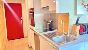 Une cuisine moderne avec un évier en acier inoxydable, une porte rouge et un îlot de cuisine doté d’une bouilloire et d’un range-couteaux.