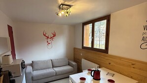 Une pièce chaleureuse avec une tête de lit en bois, une table blanche avec des tasses rouges, un canapé gris et une décoration murale représentant une tête de cerf.