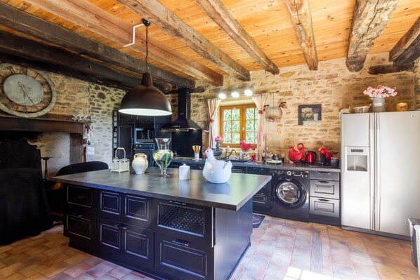 A rustic kitchen with a stone wall, wooden beams, a large island with a sink, and a built-in oven.