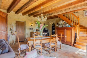 A rustic interior with a wooden dining table, chairs, a sofa, a staircase, and a chandelier.
