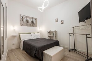 Une chambre à coucher comprenant un lit, des tables de chevet, un banc, une télévision, une étagère murale et un porte-vêtements.